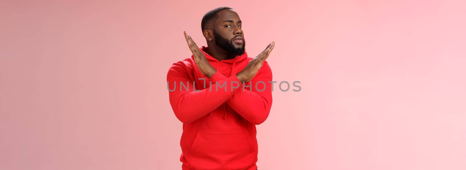 Cut it out. Portrait serious-looking african american male assisant show cross gesture say finish refusing, rejecting offer never gonna do it, standing reluctant pink background negative answer.