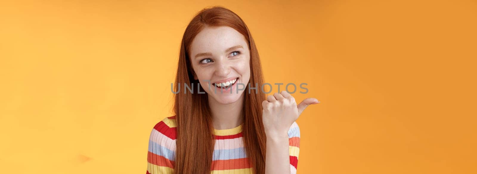 Amused outgoing redhead stylish female student discuss girly things smiling cheeky pointing handsome guy smirking devious pointing thumb looking intrigued curiously staring orange background by Benzoix
