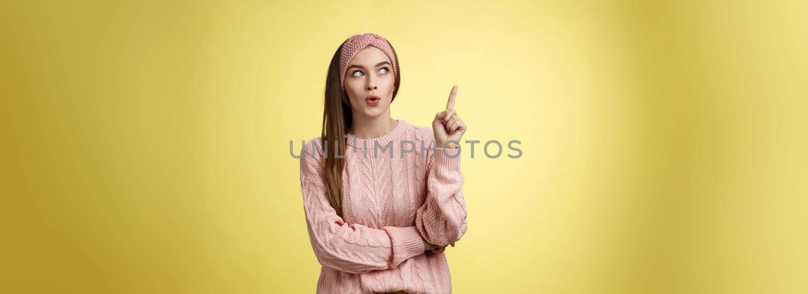 Lightbulb, I have idea. Amused and enthusiastic creative young female project manager raising index finger, showing eureka gesture folding lips intrigued looking up suggesting plan came to mind by Benzoix