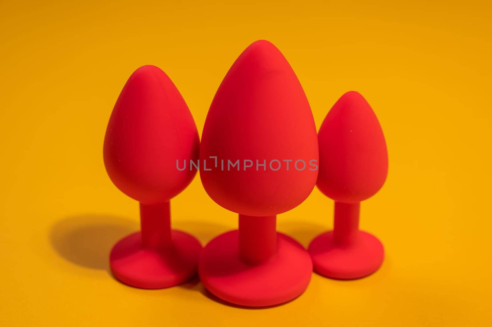 Three size silicone red butt plugs on an orange background. by mrwed54