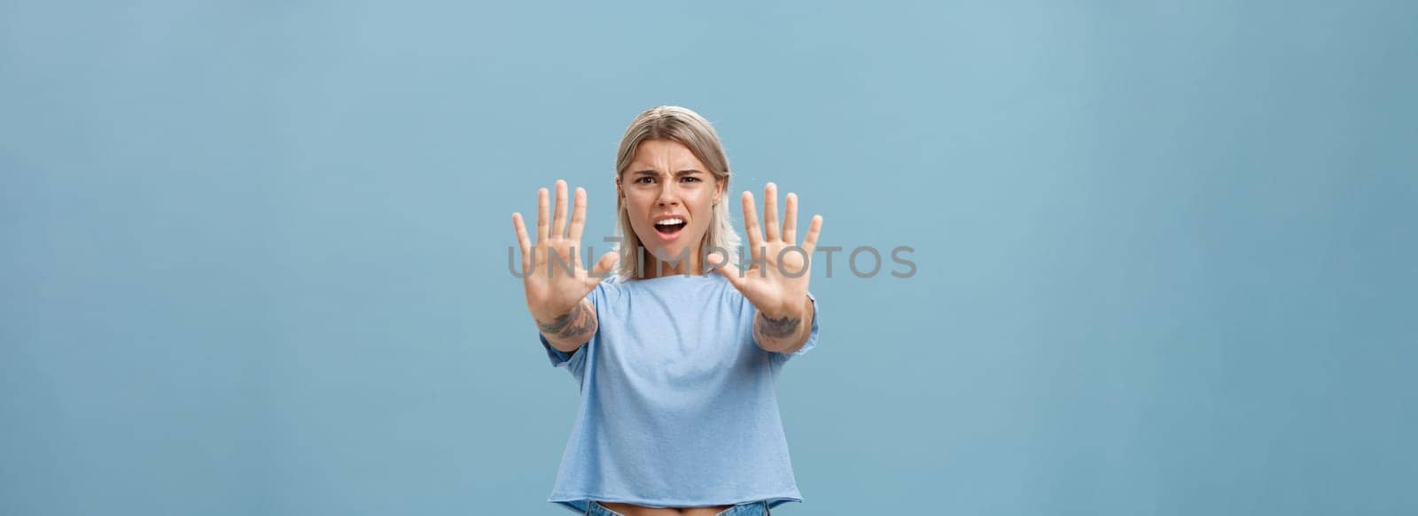 Hold right there. Portrait of intense displeased and irritated attractive young female in blue t-shirt pulling hands towards camera in stop or not gesture frowning and making annoyed expression.