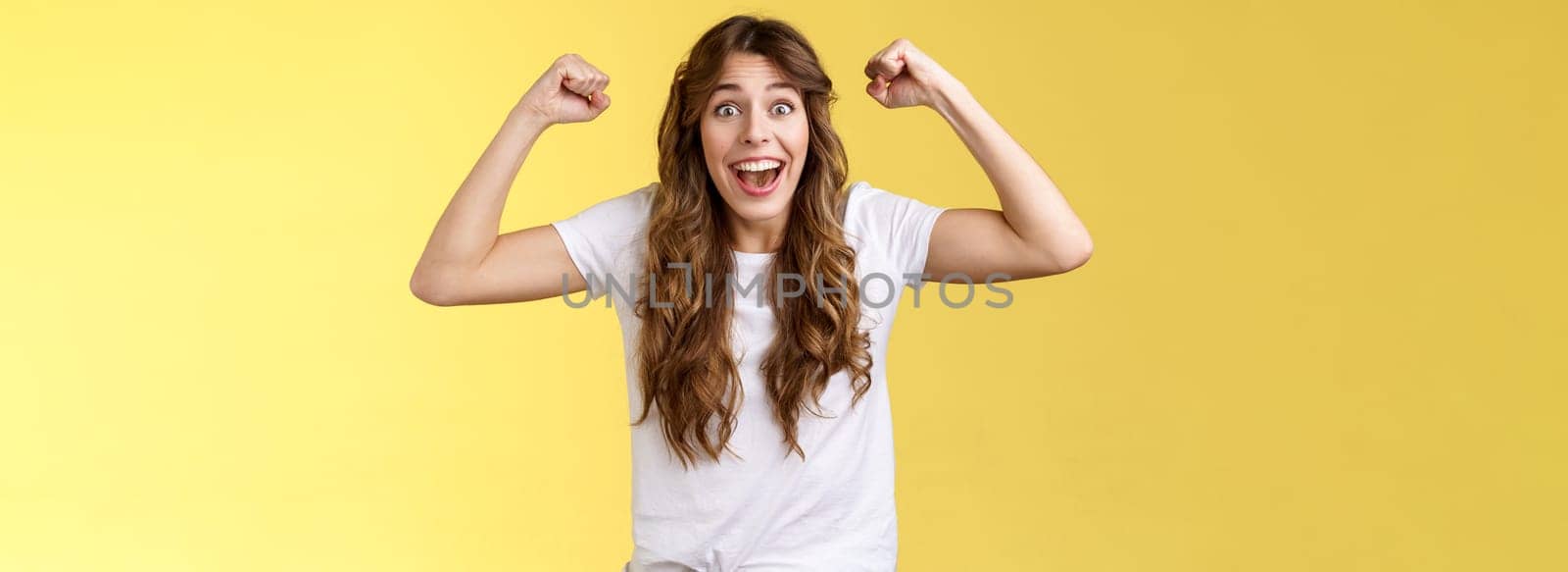 Lucky girl feeling like winner. Triumphing excited cheerful young woman raise hands fist pump up celebratory smiling broadly thrilled yelling supportive root favorite team reach success.