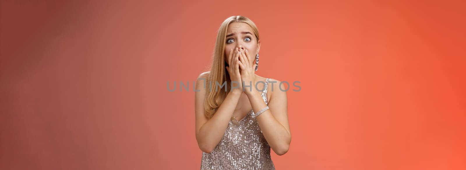 Shocked afraid insecure terrified unconfident concerned young blond woman in silver stylish dress gasping horrified pop eyes stunned red background look afraid, panicking witness crime by Benzoix