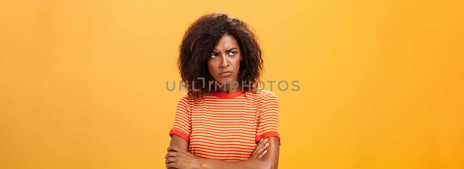 Why life so cruel and unfair. Gloomy displeased and sad cute african american young woman with curly hairstyle crossing arms on chest in offended pose frowning looking left jealous and unhappy.