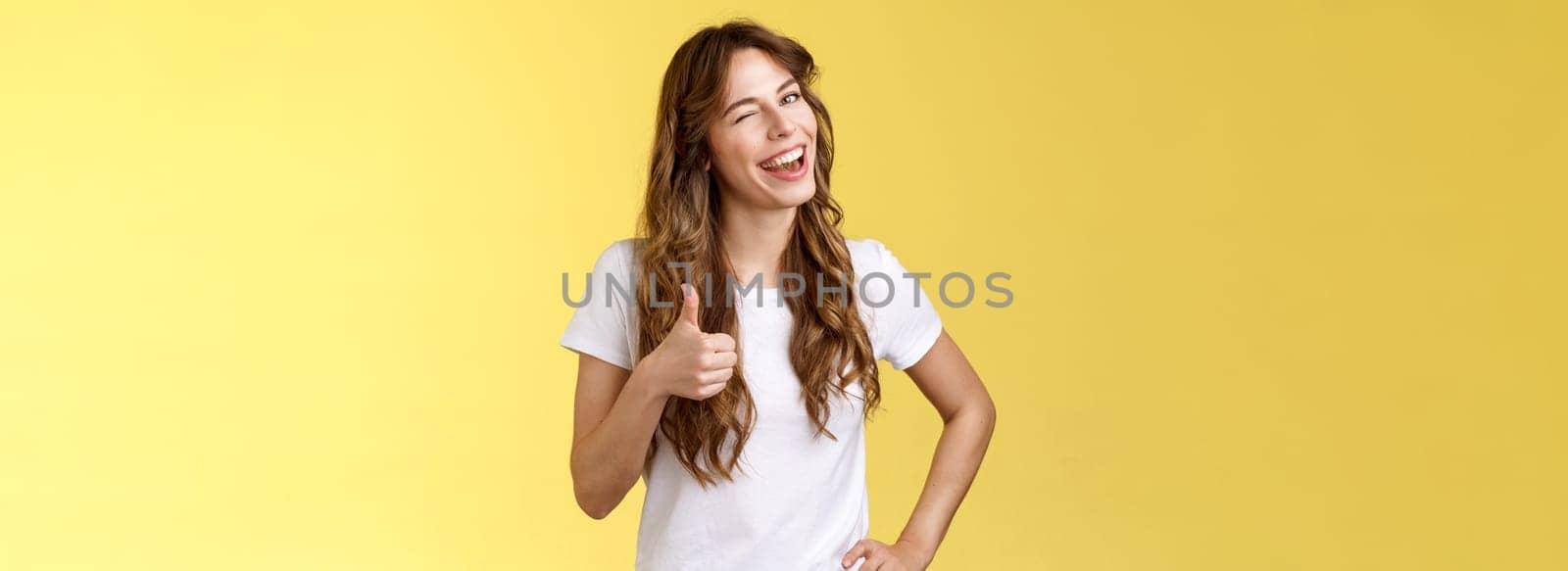 I support you guys good luck. Happy cheerful cheeky attractive girl wink approval like show thumb up smiling broadly satisfied awesome party congratulating friend well done yellow background.