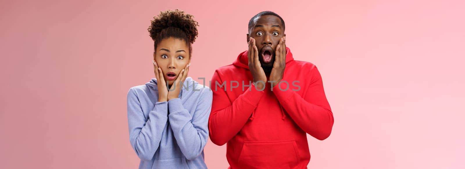 Amazed shocked gasping speechless two african american man woman drop jaw press palms cheeks worried nervous sympathizing terrible story standing stunned imrpessed pink background, feel sorry.