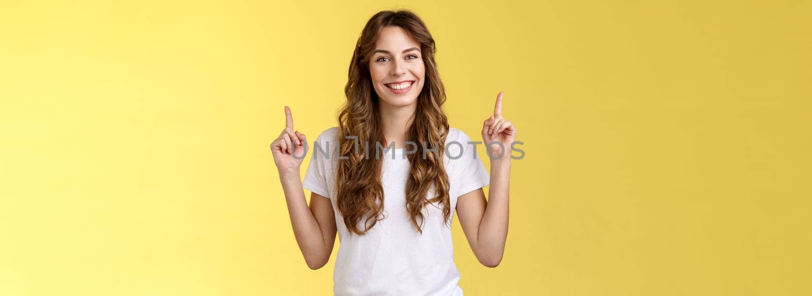 Self-assured confident lively charming european tall girl showing advicing cool promo pointing up index fingers smiling toothy delighted introuce excellent choice advertisement yellow background.