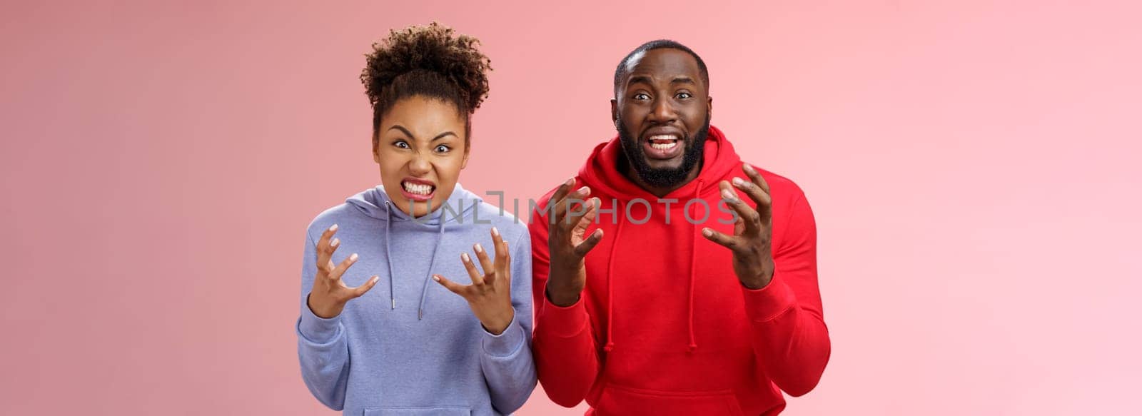 Two siblings upset failure losing bet watching football match cringing sorrow reckless, raising hands dismay sadness express regret anger being disappointed, standing pink background distressed.