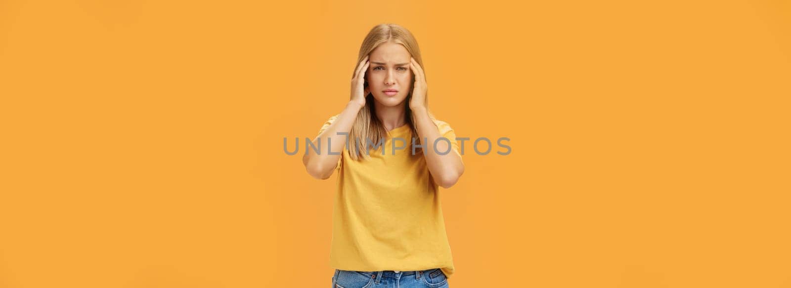 Portrait of drained sad young woman with tanned skin and fair hair feeling discomfort in head touching temples squinting and looking sick suffering headache or migraine trying concentrate on work. Copy space