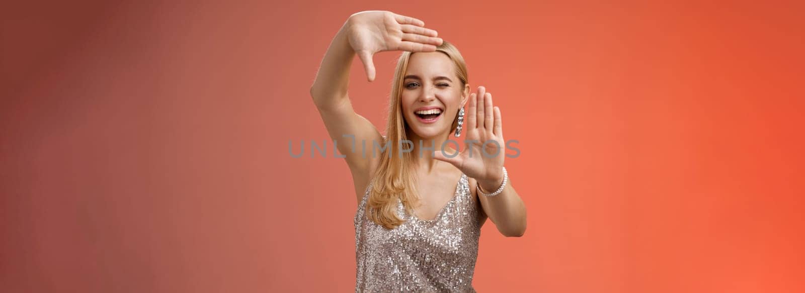 Sassy good-looking creative european blond woman in silver glittering dress winking cheeky smiling confident search inspiration around make frame hand search location take cool shot, red background.