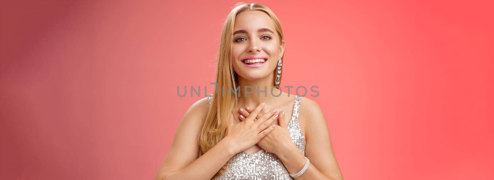 Grateful charming blond european 25s woman in silver party dress press palms heart feel thankful appreciate effort cherish romantic gesture receive flattering compliments gifts, smiling happily.
