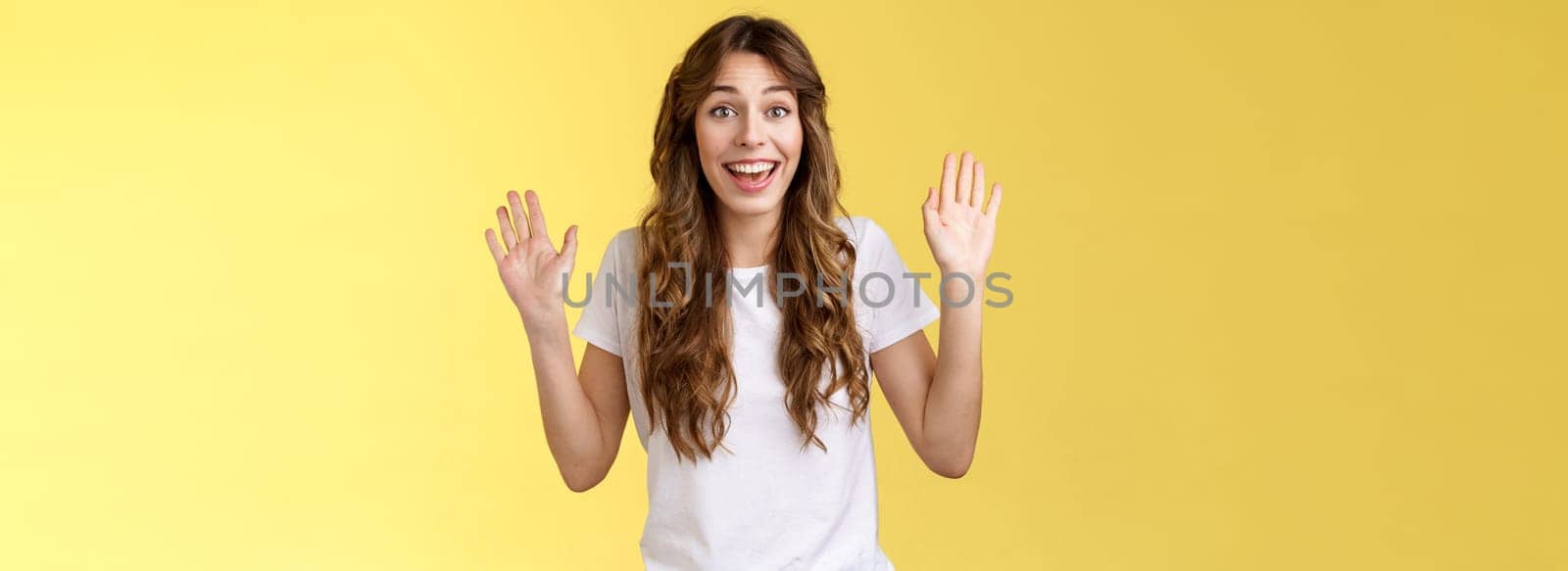 Cheerful glad outgoing cute positive young girl smiling broadly raise both palms waving hands hello greeting gesture welcome friend guest smiling hi gladly invite come inside yellow background. Lifestyle.