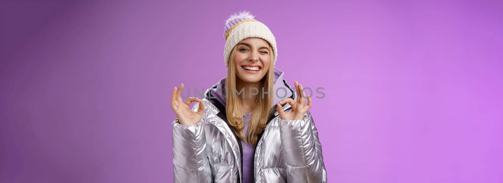 Sassy attractive blond girl in outdoor stylish jacket hat hoodie show no problem okay perfection gesture satisfied good hotel quality smiling broadly winking cheeky camera, enjoying holidays.