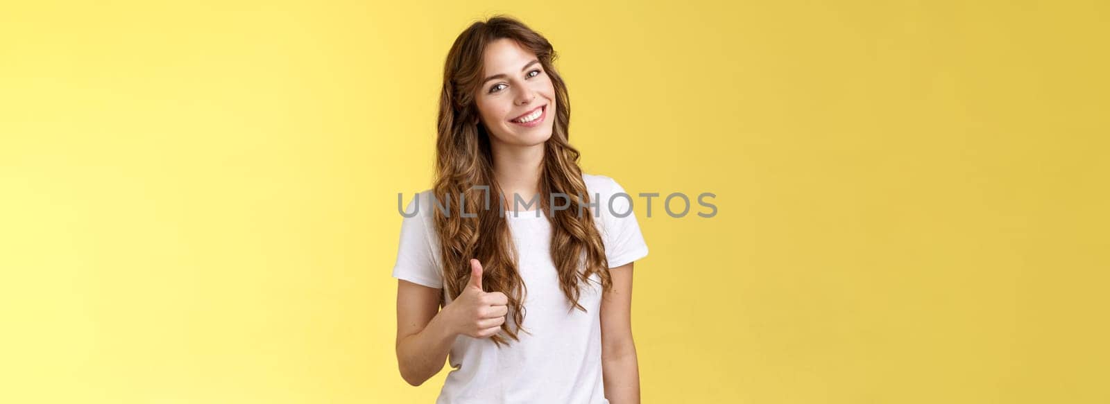 Well done congratulations. Happy charismatic pretty european female tilt head smiling broadly accept agree your idea like satisfied good result show thumb up approval gesture yellow background by Benzoix