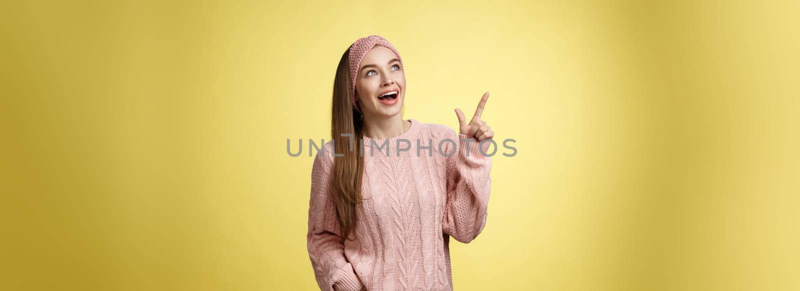 Amused and impressed dreamy pretty young european woman in knitted sweater gasping entertained dropping jaw smiling thrilled, joyful, pointing, looking at upper left corner excited of awesome promo.