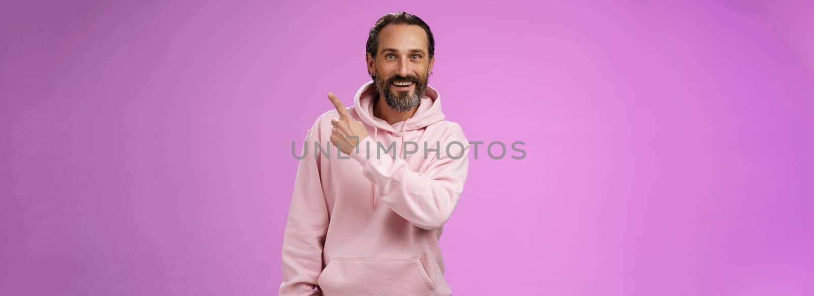 Good-looking lucky energized happy mature 50s man grey hair in trendy hipster hoodie pointing upper right corner amused telling you interesting news smiling white teeth thrilled joyfully look camera. Lifestyle.