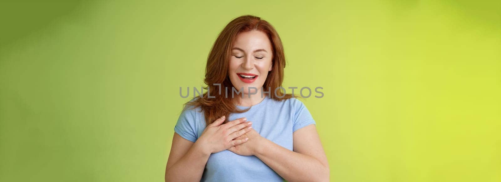 Fascinated cute redhead passionate middle-aged woman sighing lovely touch heart close eyes smiling delighted express admiration temptation feeling appreciation grateful emotions green background by Benzoix