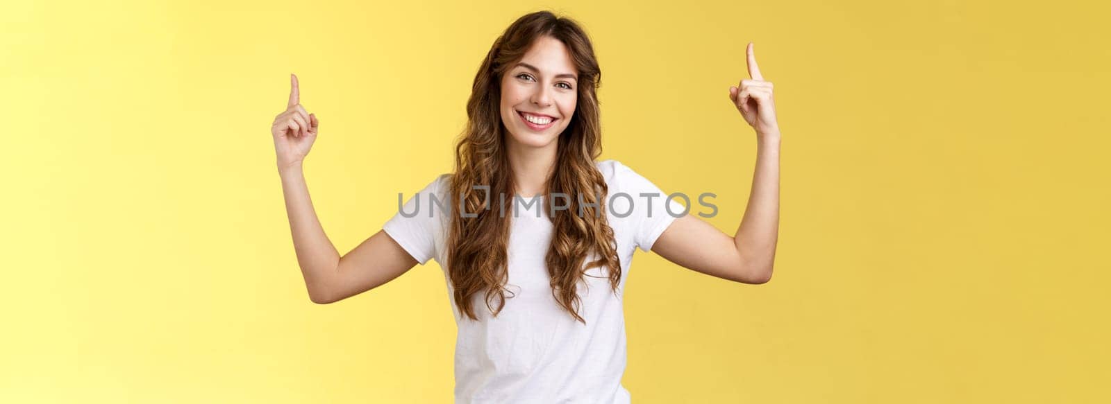 Friendly charismatic good-looking woman showing you great promo place pointing up index fingers raised top copy space smiling toothy delighted tilt head introduce advertisement great choice. Lifestyle.