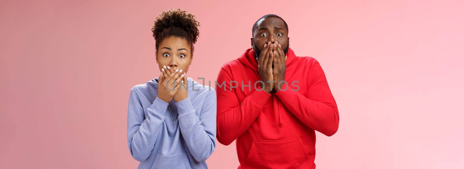 Two shocked african-american man woman widen eyes concerned terribly sorry press palms mouth gasping witness disaster hear sad bad news, standing worried pink background sympathizing friend.