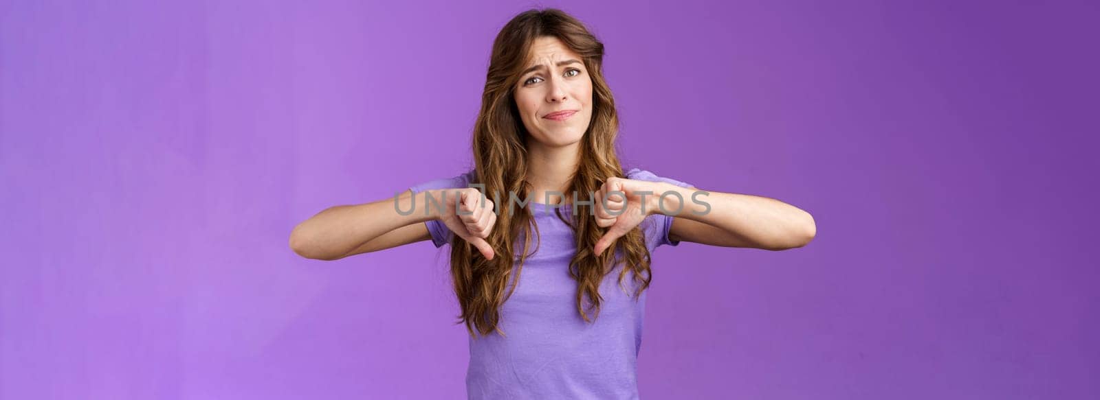 Disappointed displeased pity girl show thumbs down grimace dislike express negative opinion thumbs down gesture apologizing giving bad feedback stand purple background unimpressed.