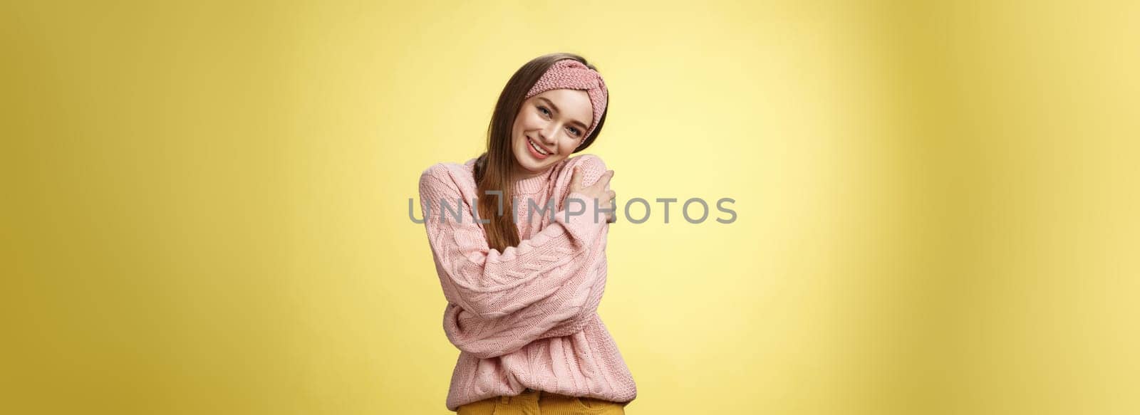 Girl feeling warm and safe thanks charming boyfriend embracing herself romantically hugging leaning on shoulder enjoying warmth of fluffy sweater, smiling tender in love over yellow background.