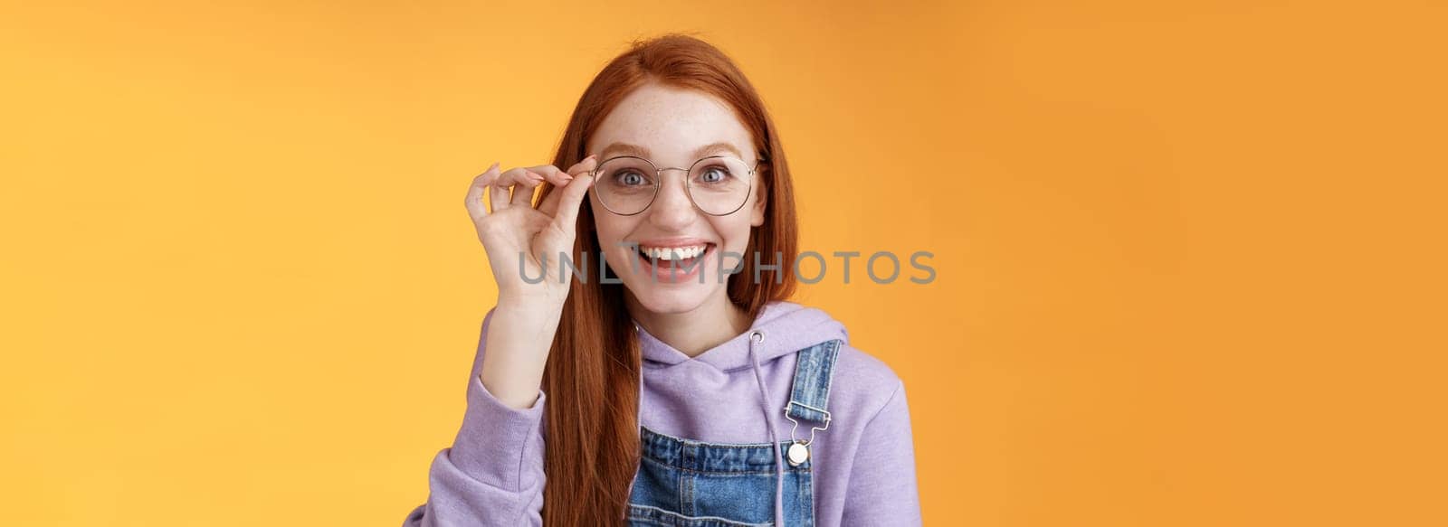 Happy enthusiastic young redhead girl amused find out excellent place celebrate b-day standing joyful excited touch glasses smiling broadly white teeth grinning rejoicing surprised, orange background.