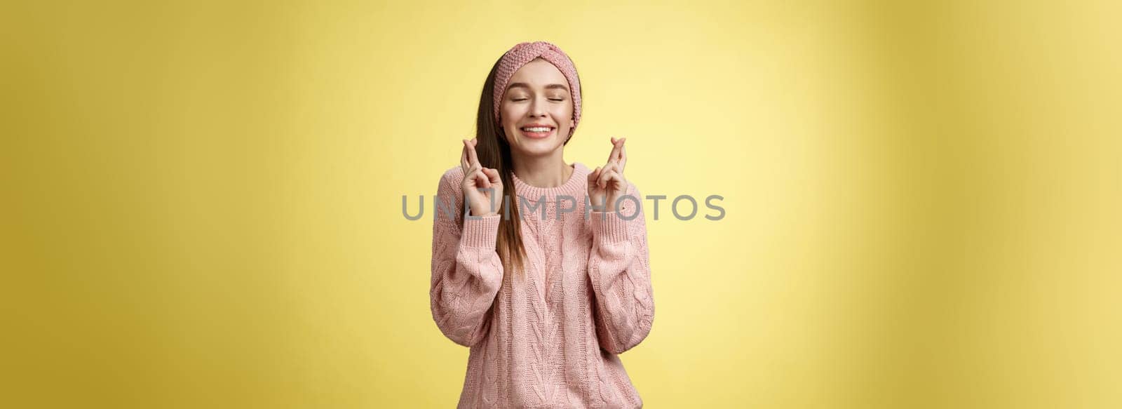 Girl wishing wellness wanting dream come true, cross fingers dreamy, close eyes waiting miracle, anticipating good news, posing excited and joyful against yellow background in knitted warm sweater by Benzoix