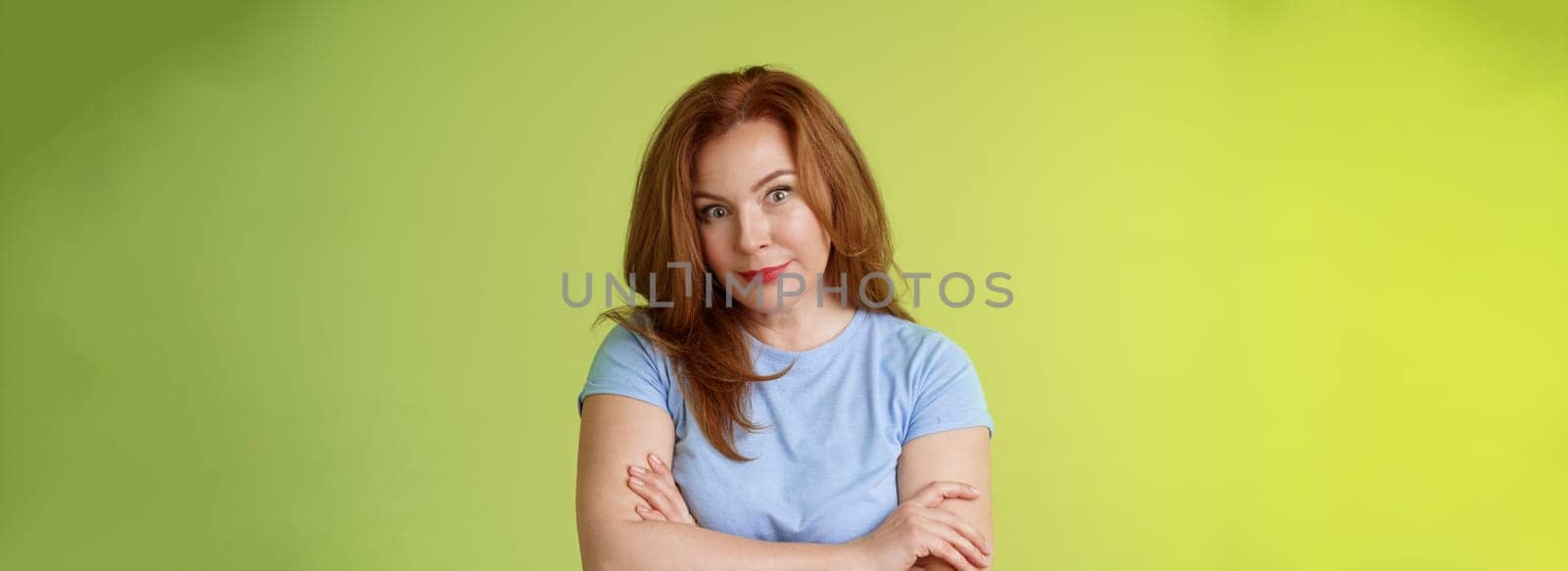 Confused shocked redhead mother look serious worried puzzled cross arms chest. self-soothing calming gesture stare camera perplexed frustrated bad son behaviour stand green background disappointed.