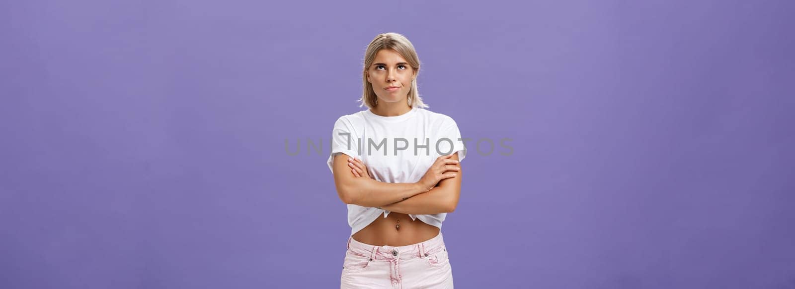 Lifestyle. Girl being irritated waiting for appointment sighing rolling eyes up from annoyance crossing hands over body and smirking from impatience and dissatisfaction standing intense over purple wall.