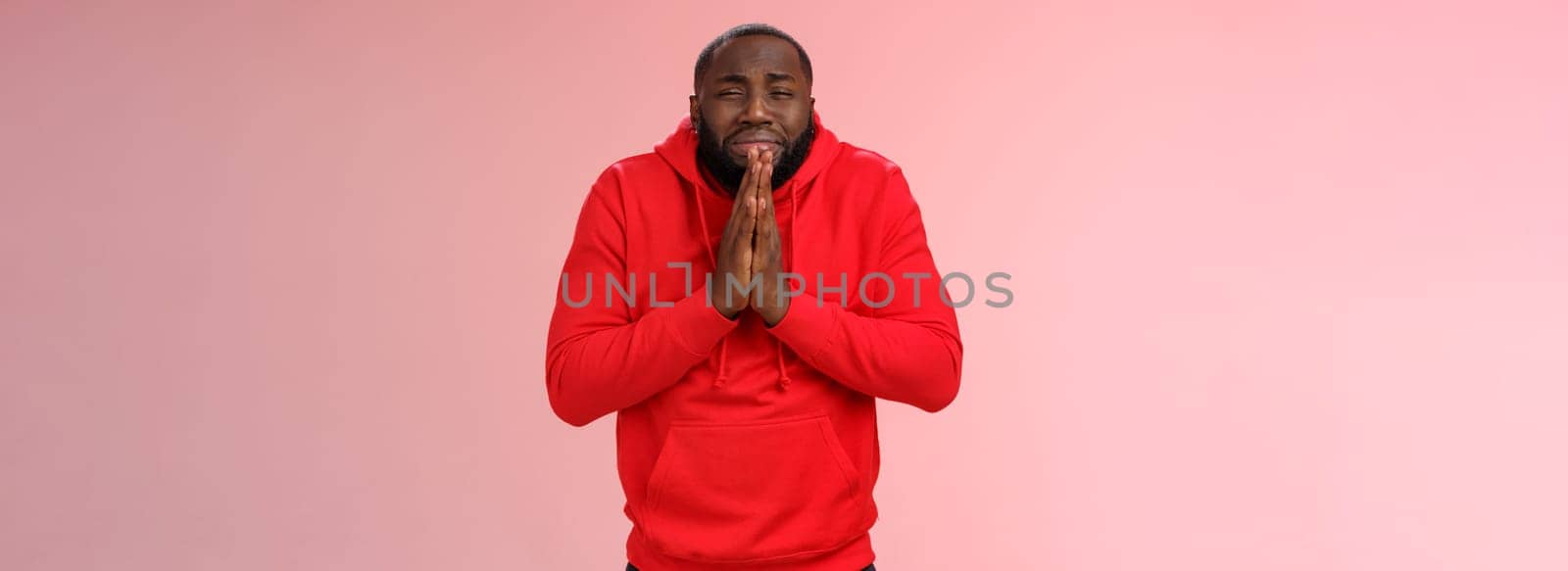 Miserable african american man beard in red hoodie stooping make supplicating upset grimace grying sobbing asking help say please hold hands pray begging mercy, apologizing need money.