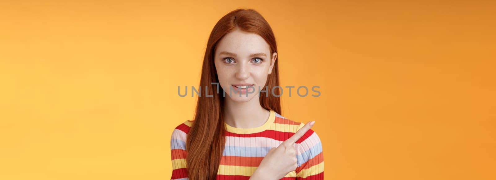 Lifestyle. Curious smart female redhead coworker asking friend who was that pointing left index finger look camera thoughtful questioned wanna know answer smiling intrigued standing orange background.