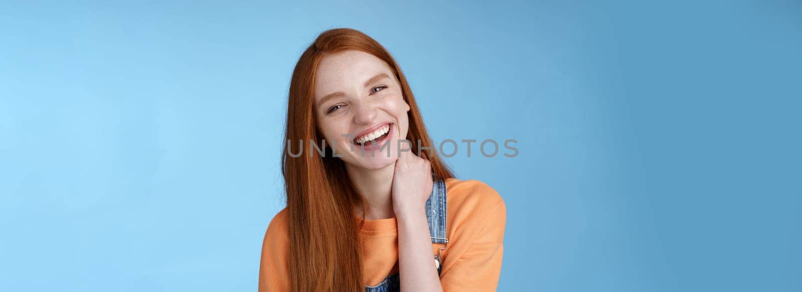 Carefree silly flirty young redhead girlfriend having fun enjoying lovely date summer evening laughing out loud smiling broadly tilting head touching neck shy blushing acting cute blue background by Benzoix