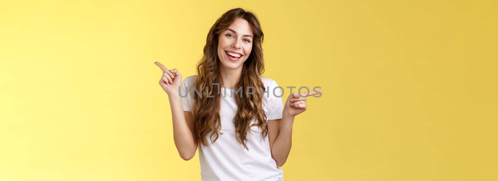 Girl have two suggestions pointing sideways. Cheerful charismatic curly-haired attractive woman pointing left right index fingers introduce promo products smiling broadly lively recommend ad.