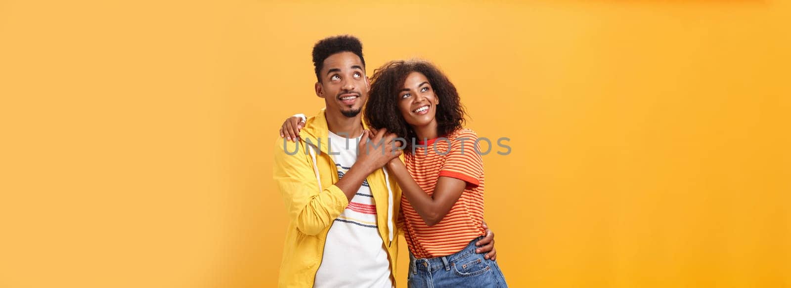 Couple of lovers enjoying spending warm summer evening together gazing up at stars with happy. enthusiastic expression being in love hugging and expressing warm romantic feelings over orange wall.