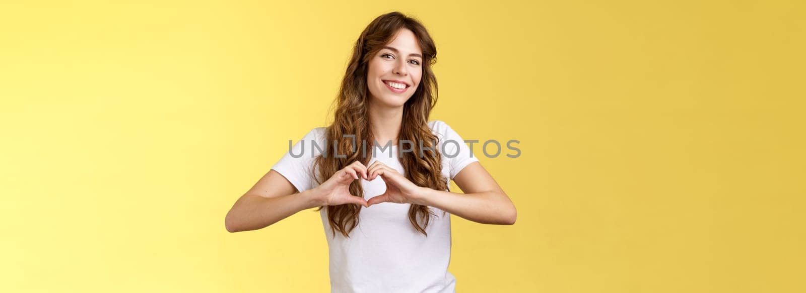 Carefree tender attractive woman curly long hairstyle show heart sign near chest express love like summer memories smiling broadly tilt head joyfully confess romantic feelings cherish friendship by Benzoix