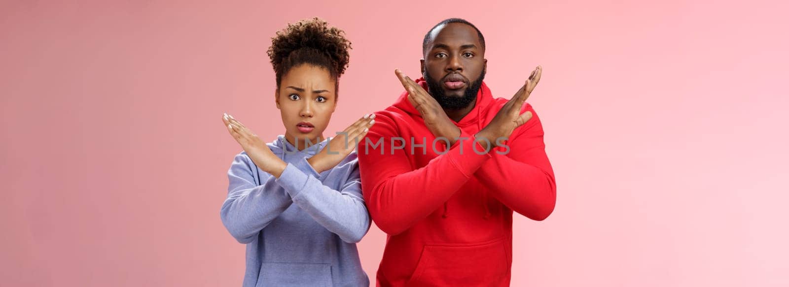 Nervous displeased two african-american man woman asking friend tell they absent not here show cross signs frowning disturbed worried begging not tell quit, stop standing pink background by Benzoix