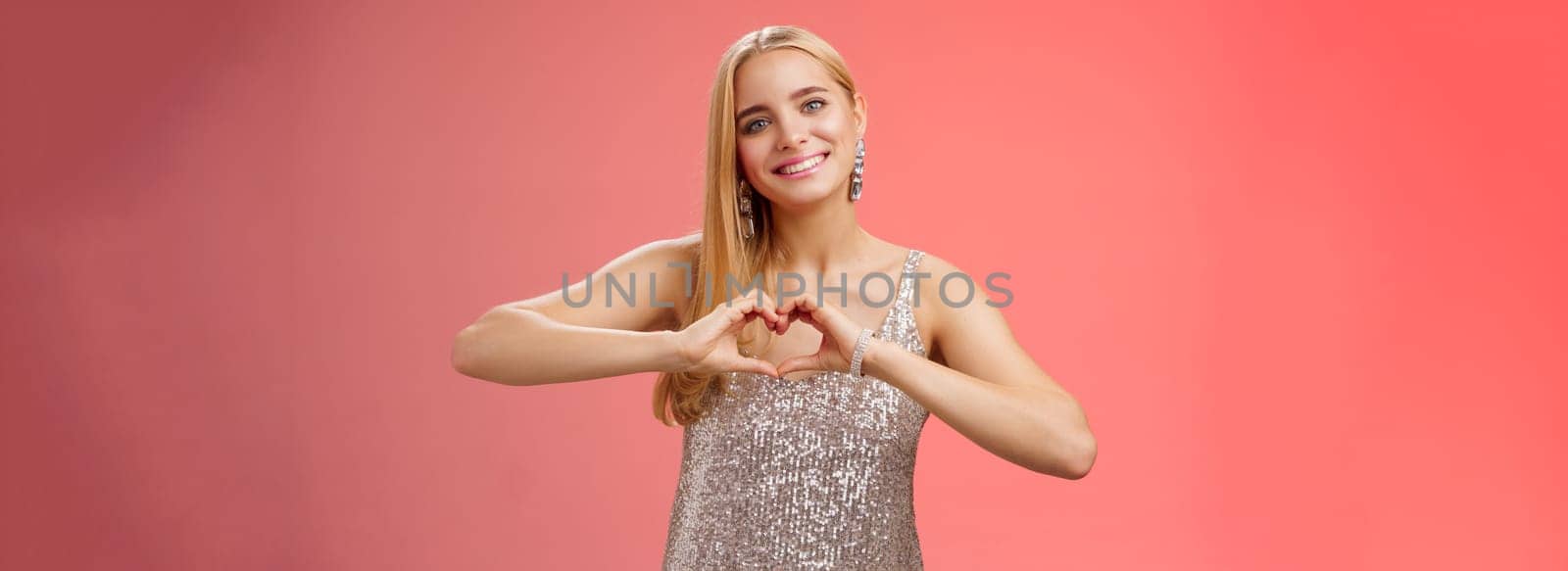 Romantic passionate charming lovely blond glamour woman in silver dress brilliants show heart love gesture express sympathy passion, adore relationship smiling delighted, standing red background by Benzoix