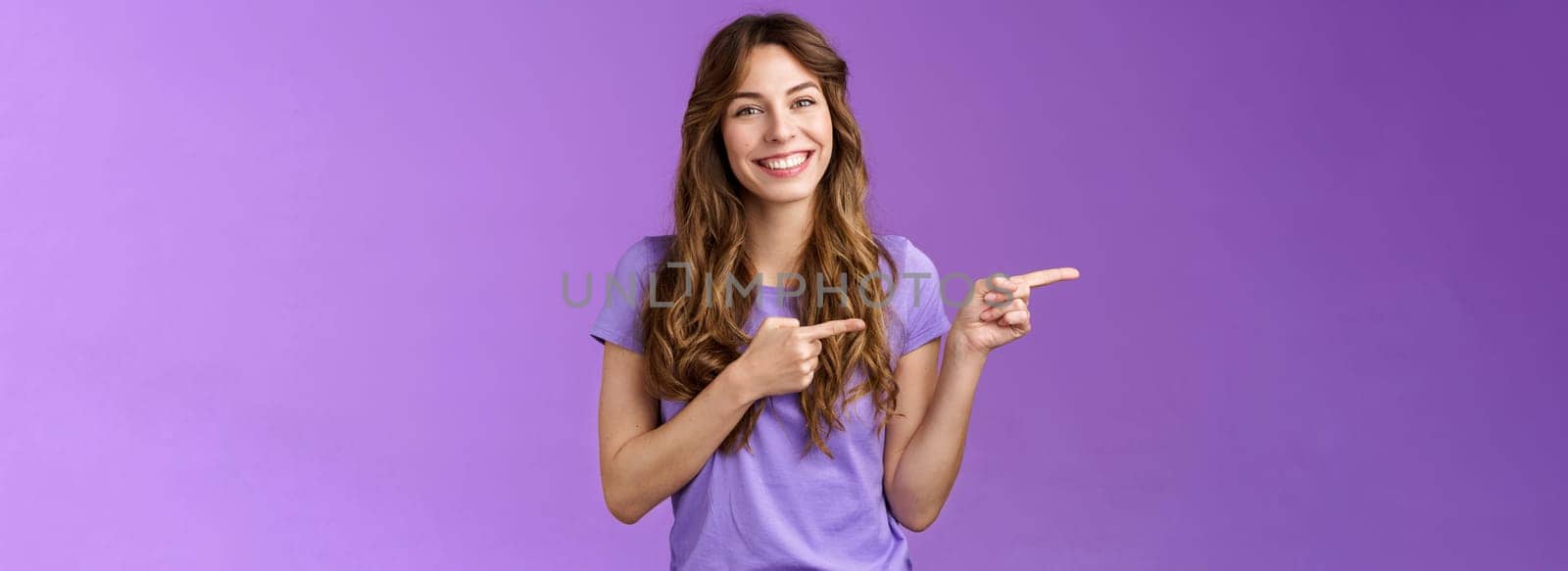You need see yourself introduce new product. Enthusiastic happy smiling toothy girl curly hairstyle promoting cool cafe menu pointing index finger left smiling broadly stand purple background.