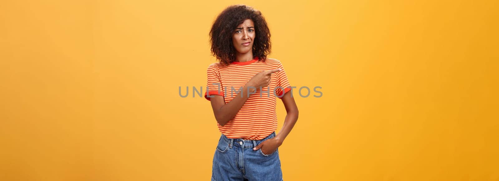 Not worth my time. Displeased unimpressed stylish attractive dark-skinned female model in striped t-shirt and denim shorts frowning with picky expression pointing left doubtful and dissatisfied. Copy space