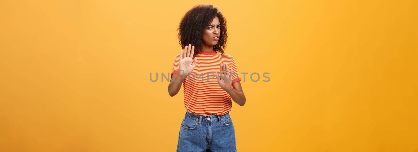 No I refuse. Intense suspicious and displeased smart african-american female rejecting bad offer pulling raised palms turning away with aversion and dissatisfied look against orange background.