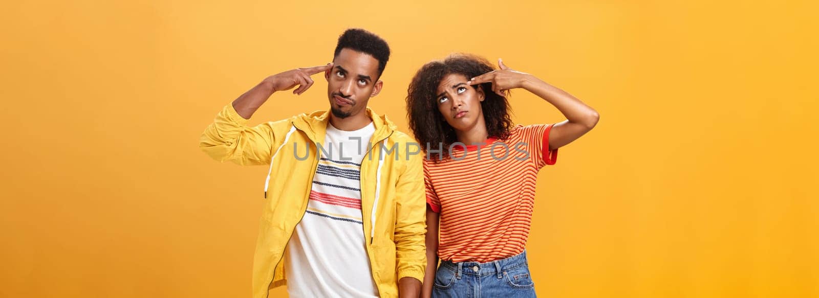 Pair of african american lovers getting annoyed with parents scolding, teaching them how live sexual life rolling eyes up from irritation holding finger gun near temples standing close to each other. Relationship concept