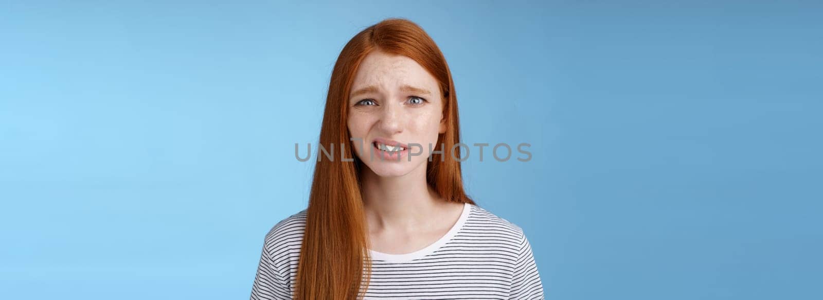 Displeased young awkward redhead girl cringe full disbelief smirking frowning confused look questioned doubtful hearing nuisance dumb story standing blue background uncertain by Benzoix