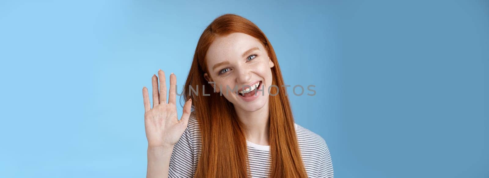 Attractive confident redhead sassy girl pure clean skin blue eyes tilting head cheerfully waving hand hello hi gesture greeting you look camera friendly welcoming friend, standing studio background.
