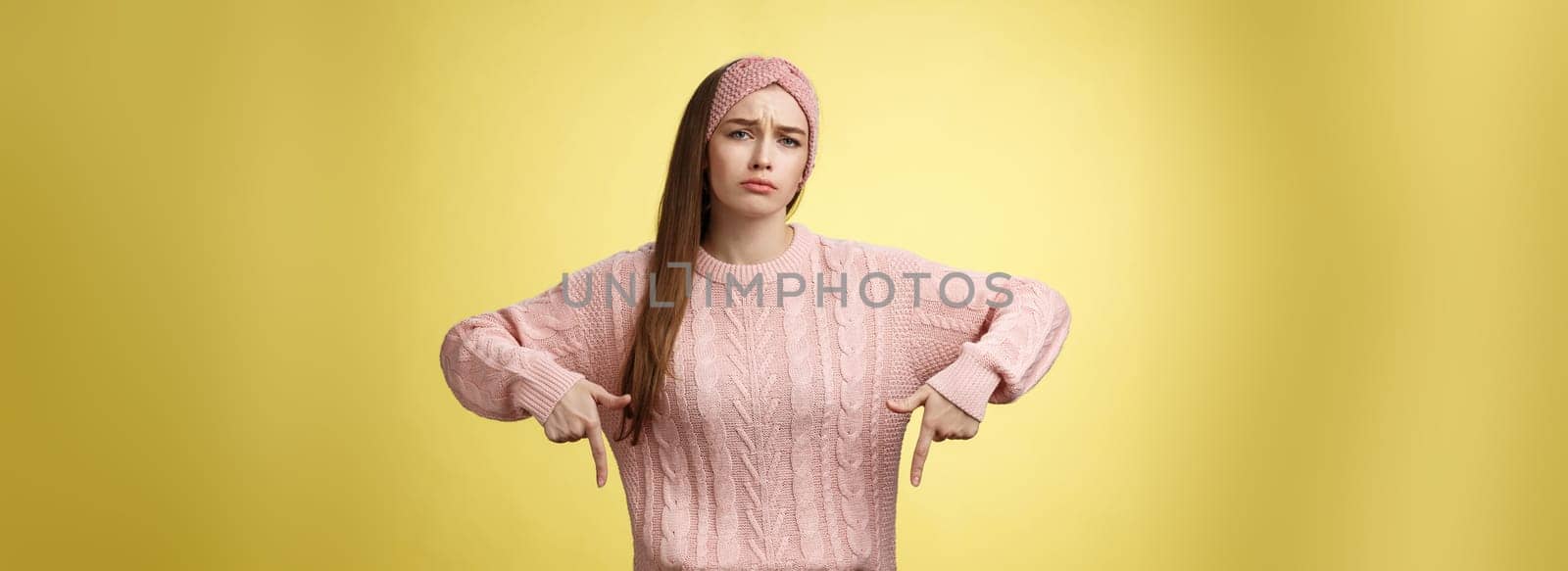 Why me, gosh. Gloomy upset complaining cute glamout young european girl in casual sweater, headband frowning, whining grimacing displeased pointing down, unhappy see lots work over yellow wall.