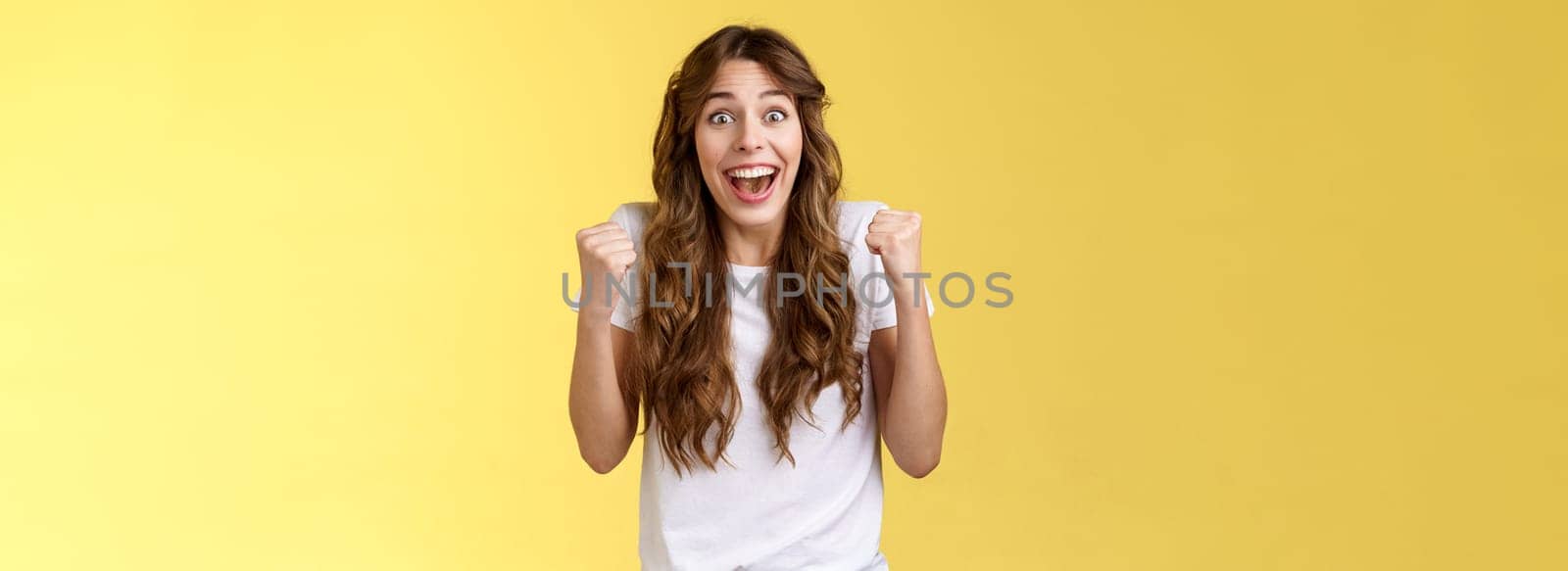 Cheerful supportive happy female fun fist pump relieved triumphing cheering rooting for favorite team winning smiling broadly hopefully look camera celebrating victory yellow background.