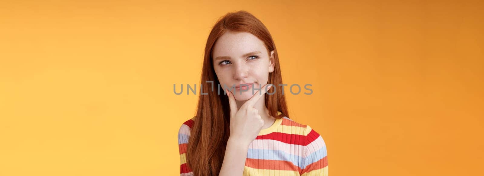 Hmm interesting. Suspicious doubtful attractive european redhead female pondering choice look hesitant thoughtful touch chin smirking tricky look upper left corner thinking, take decision by Benzoix