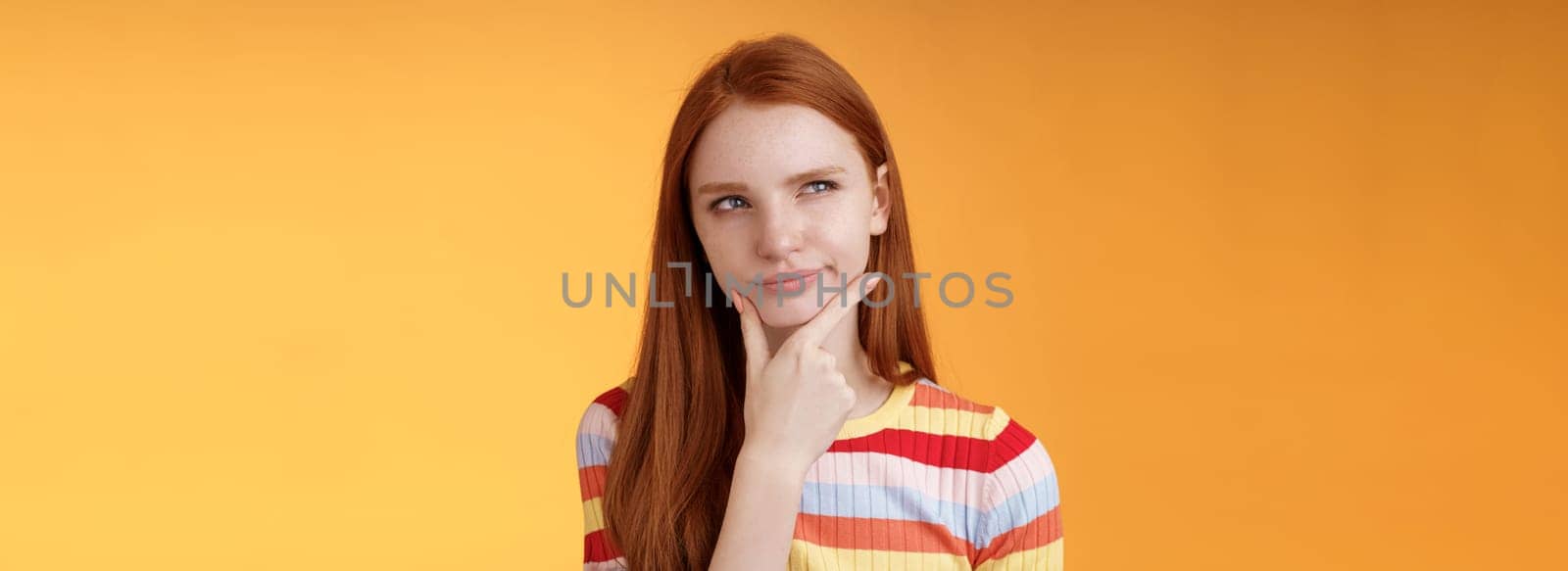 Hmm interesting. Suspicious doubtful attractive european redhead female pondering choice look hesitant thoughtful touch chin smirking tricky look upper left corner thinking, take decision.