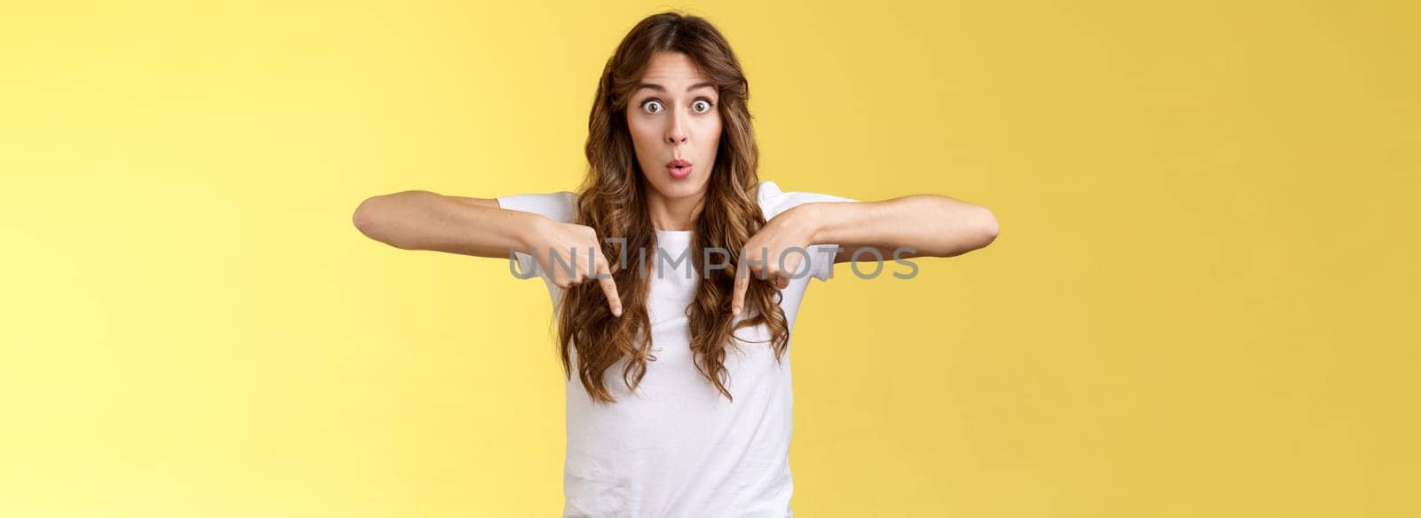 You see that too. Surprised wondered amazed happy astonished funny cheerful girl long curly haircut stare impressed amazed pointing down react fascinated curious bottom promo yellow background.