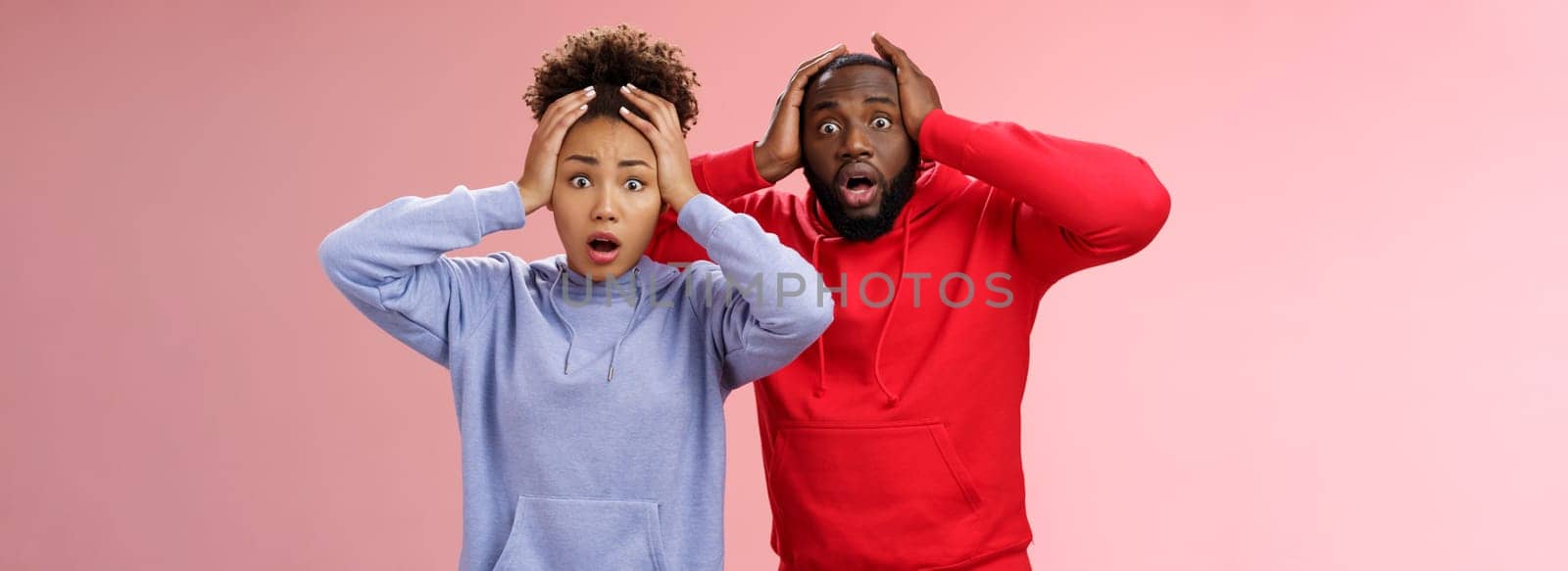 Shocked worried african american couple man woman holding hands head panicking widen eyes stunned receive bad concerning news feel troubled nervous, standing pink background anxious.