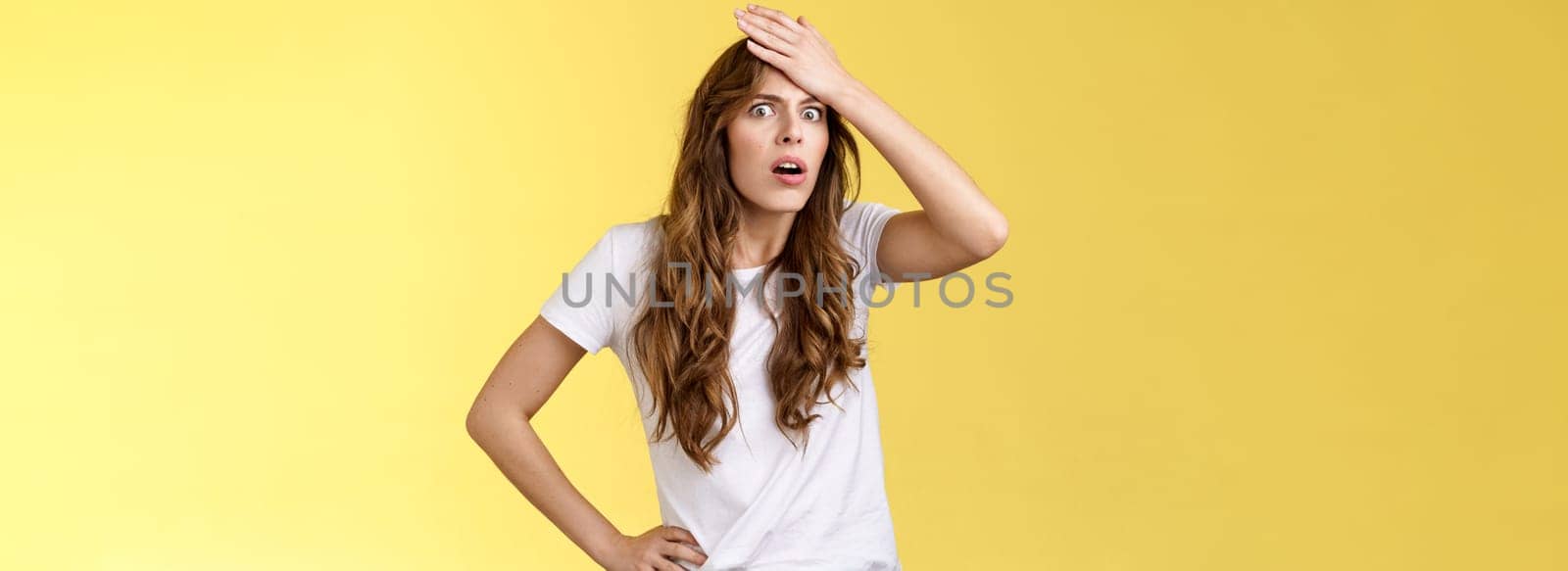 Troubled distressed bothered shocked curly-haired girl realising make stupid mistake punch forehead gasping cringe grimace bothered facepalming upset remember important task. Copy space